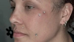 sideway of a woman's face with dermal, monroe, dimple, and lobe piercings. 