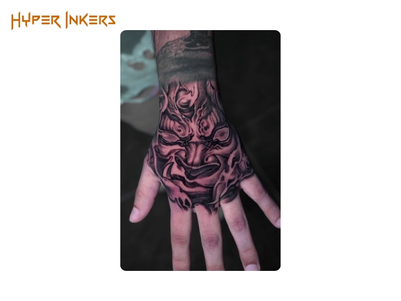 Black and grey hannya mask tattoo covering the entire back of one hand