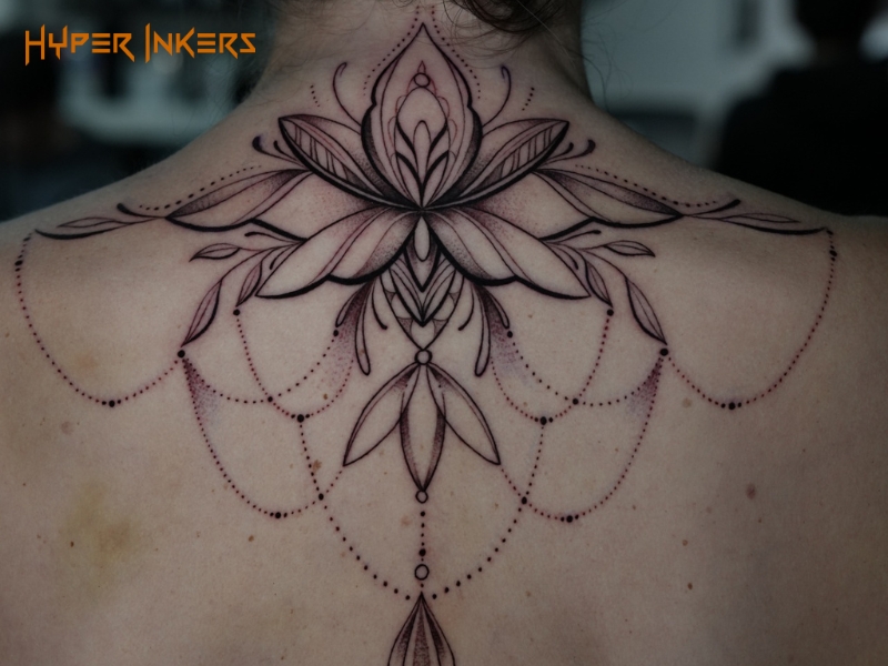 Ornamental tattoo of a symmetrical lotus with filigree chains draped across the upper back